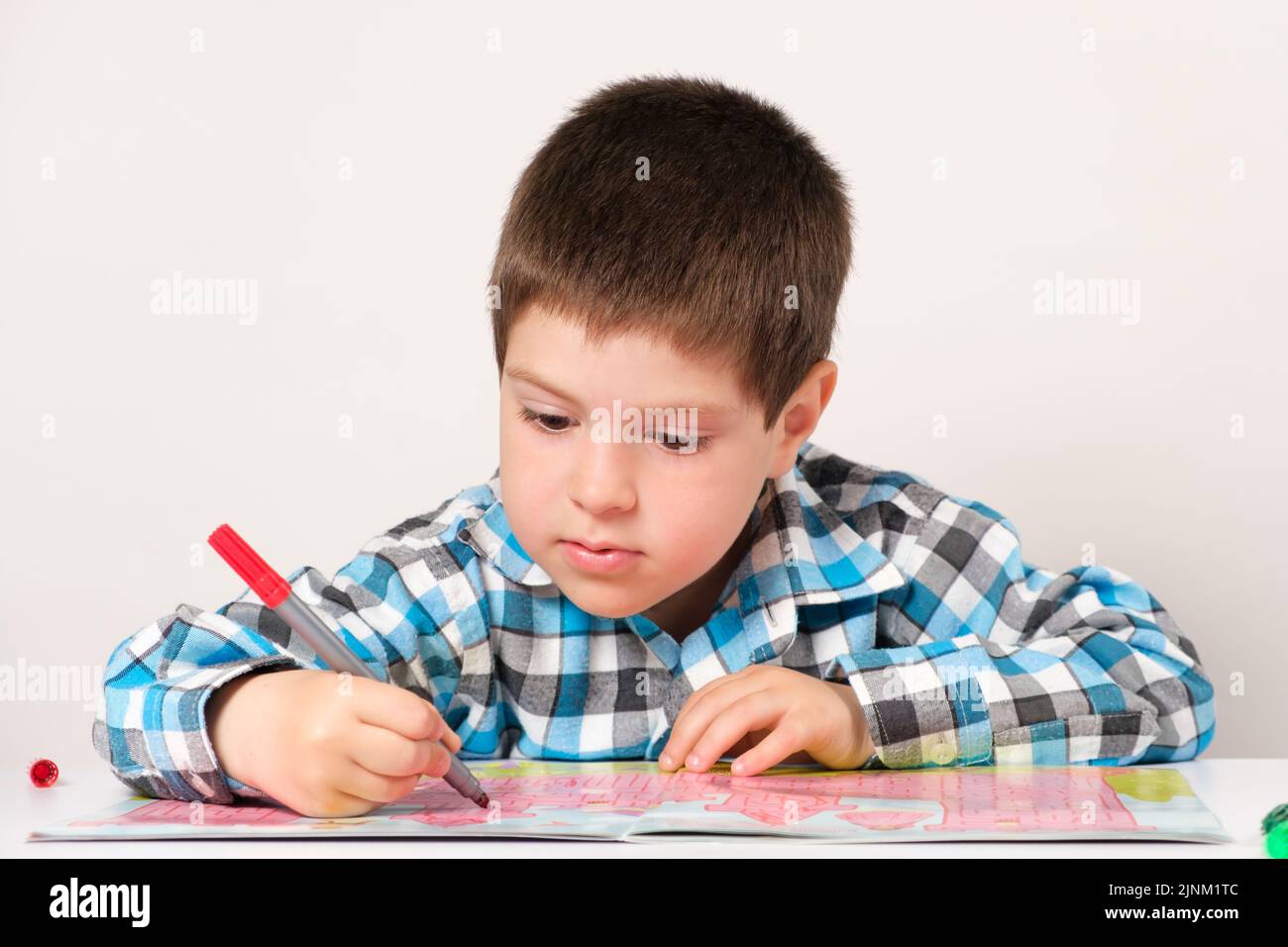 Ein Junge im Vorschulalter studiert und passiert Labyrinthe auf weißem Hintergrund. Vorbereitung für die Schule für Kinder. Stockfoto