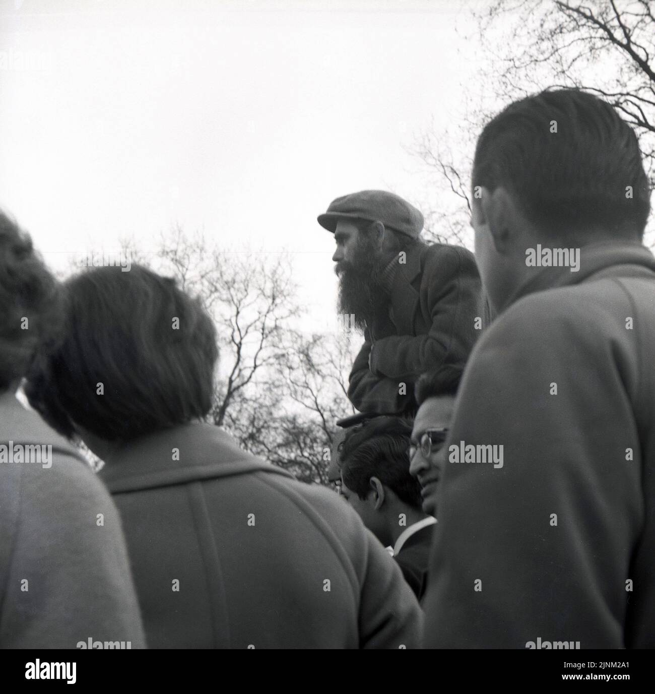 1960s, historische Menschen, die einem jungen Mann mit langem Bart zuhören und eine Mütze an den Rednercorner's im Londoner Hyde Park, London, England, Großbritannien, wetern. Stockfoto