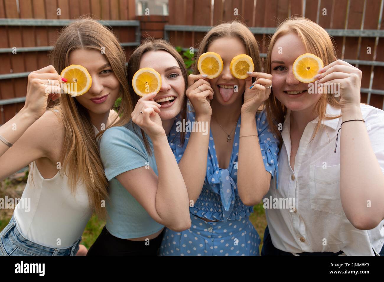 Porträt junger lachender Frauen, die die Hände ins Gesicht heben, die Augen mit Orangenscheiben bedecken, Spaß haben, scherzen. Stockfoto