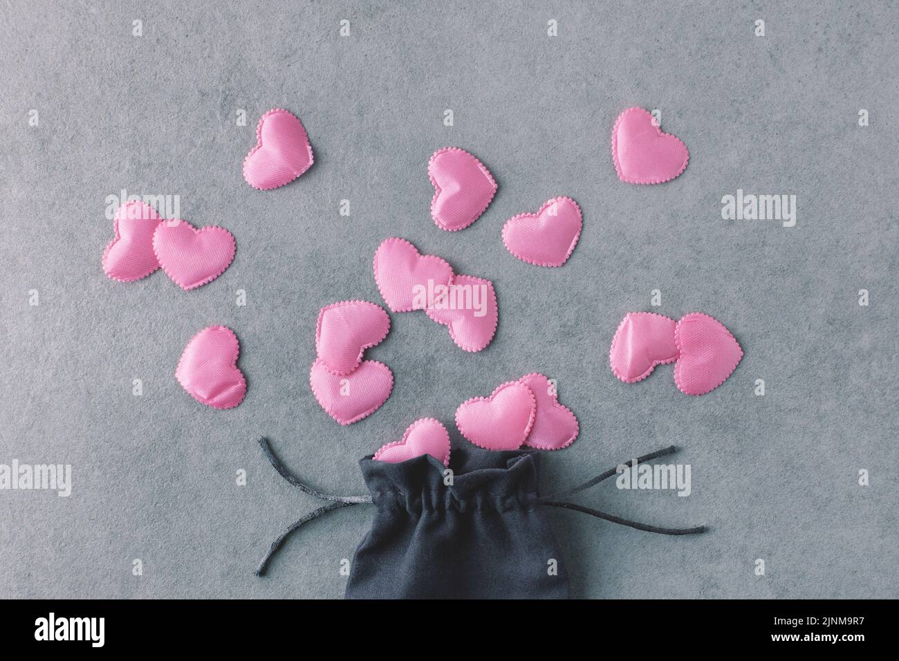 Romantisches Flatlay aus seidenrosa Herzen und Seidenbeutel auf grauem Steingrund. Liebe, Valentinstag, dekoratives Konzept. Stockfoto