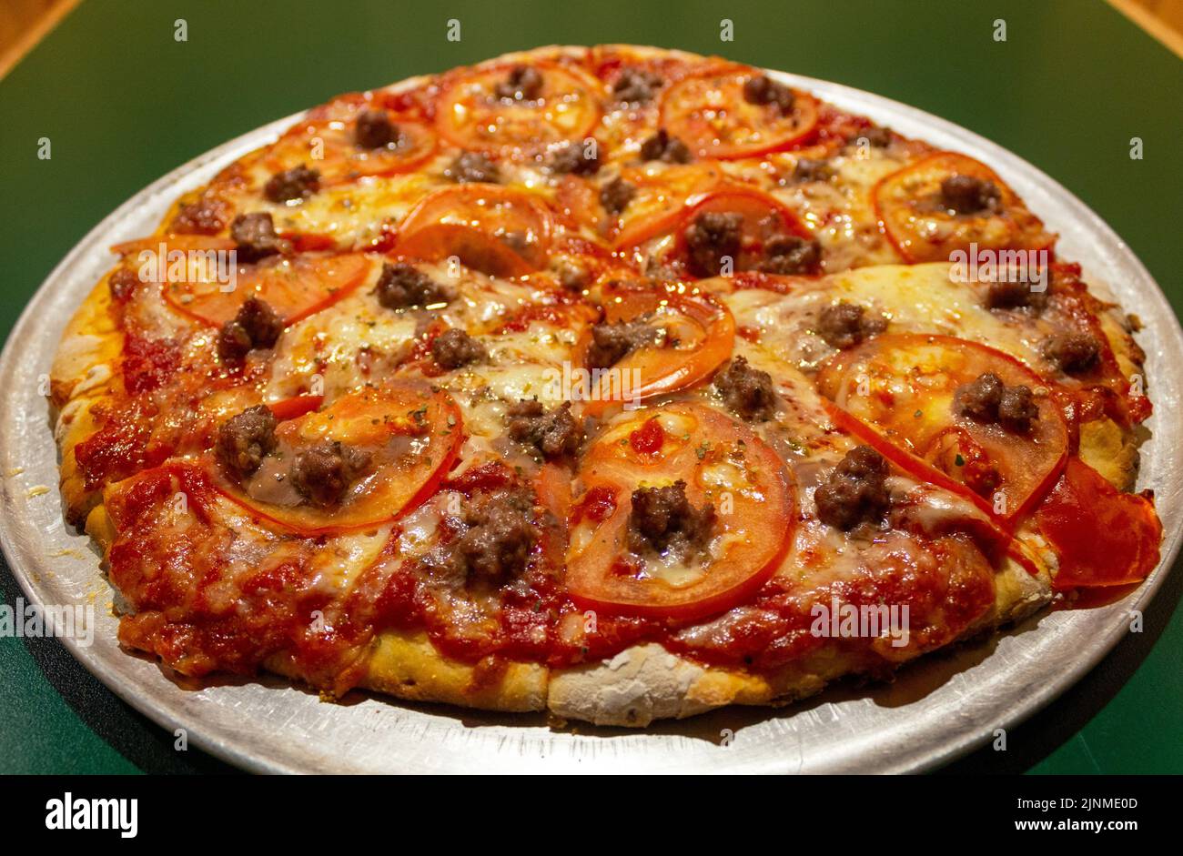 Kitschige Backsteinpizza mit Rindfleisch und Tomaten Stockfoto