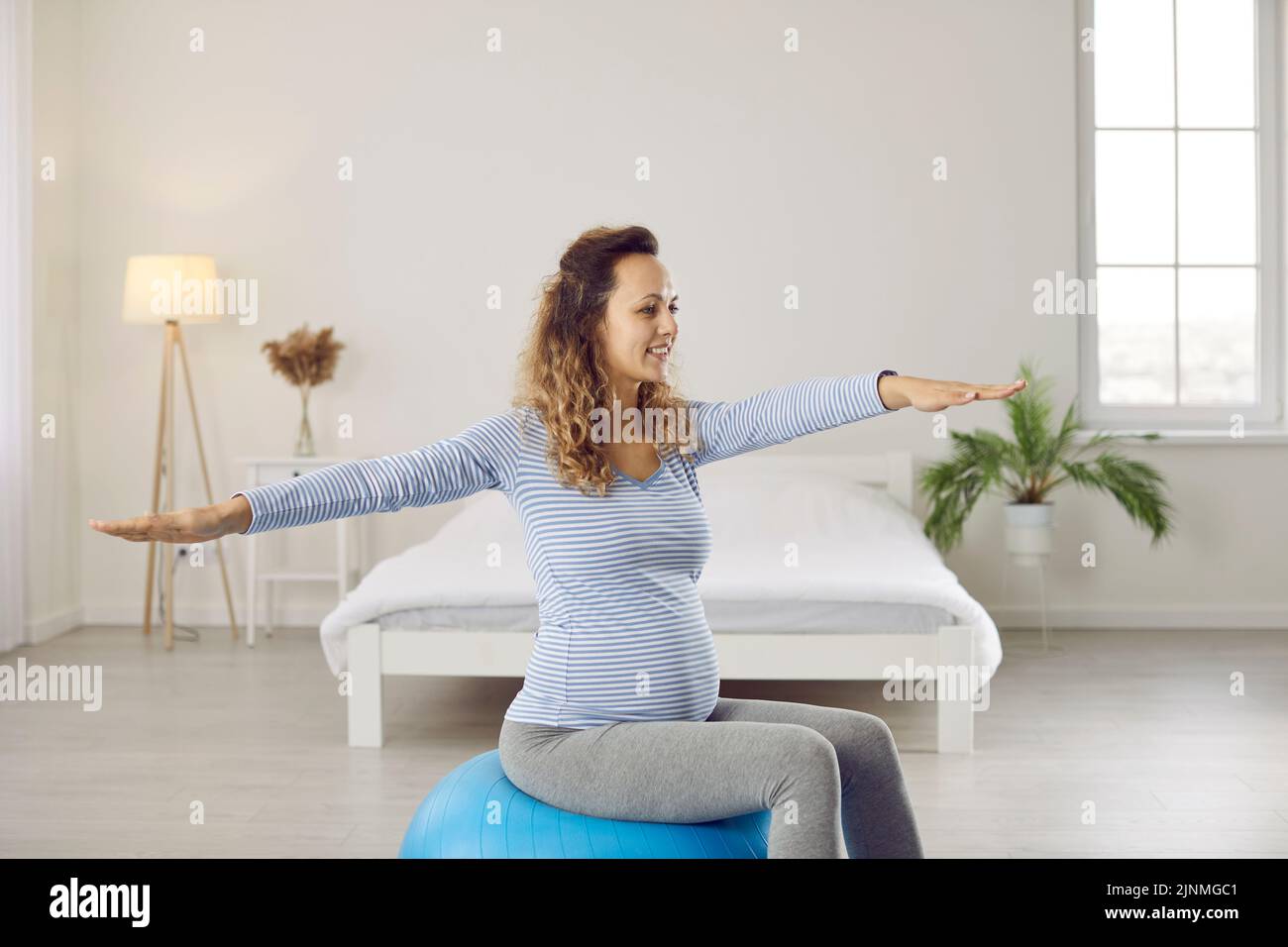 Glückliche, gesunde junge Frau, die während der Schwangerschaft Gymnastik mit einem Yoga-Ball macht Stockfoto