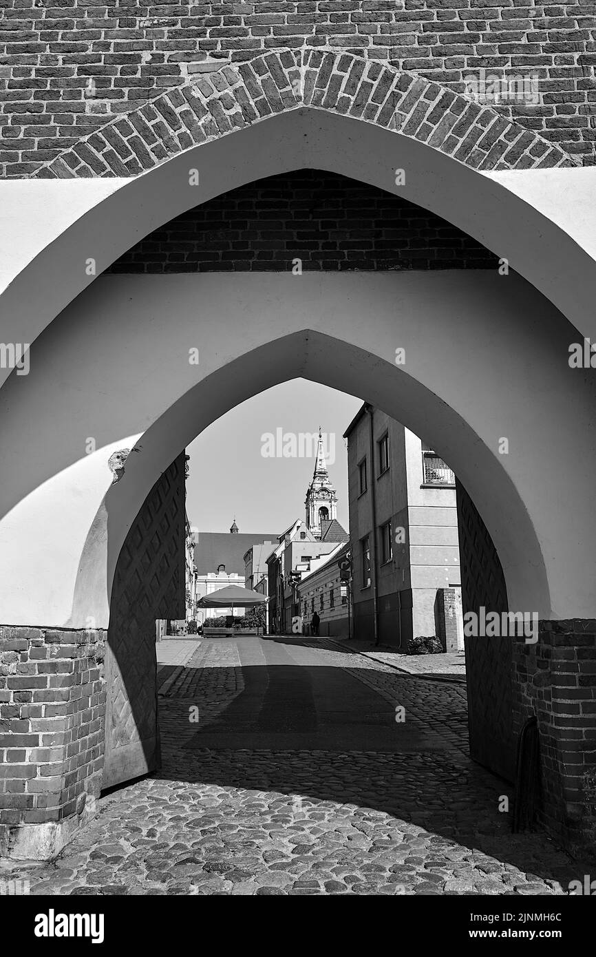 Straße und Tor in einer historischen Backsteinmauer in der Stadt Torun in Polen, monochrom Stockfoto
