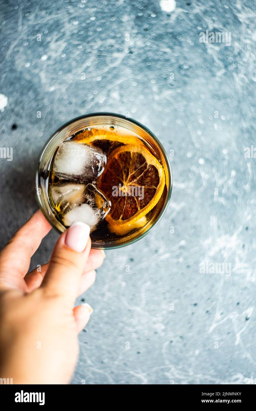 Alkoholcocktail mit Cola im Glas mit Orange und Eis in der Frauenhand Stockfoto