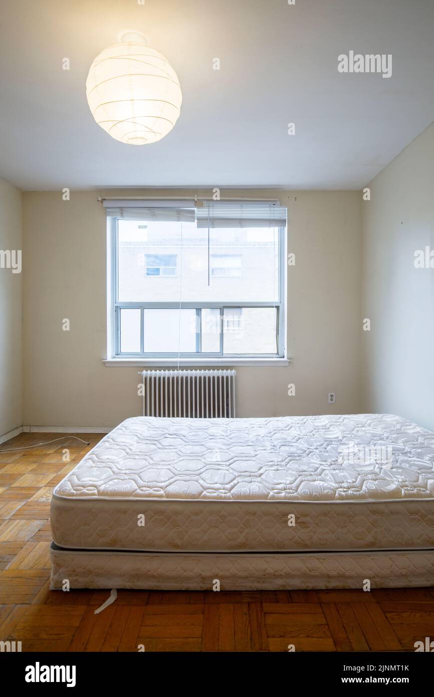 Über einer unbedeckten Matratze in einem ansonsten leeren Schlafzimmer hängt ein Papier-Pendelleuchte. Dieses Gebäude wurde seitdem abgerissen Stockfoto