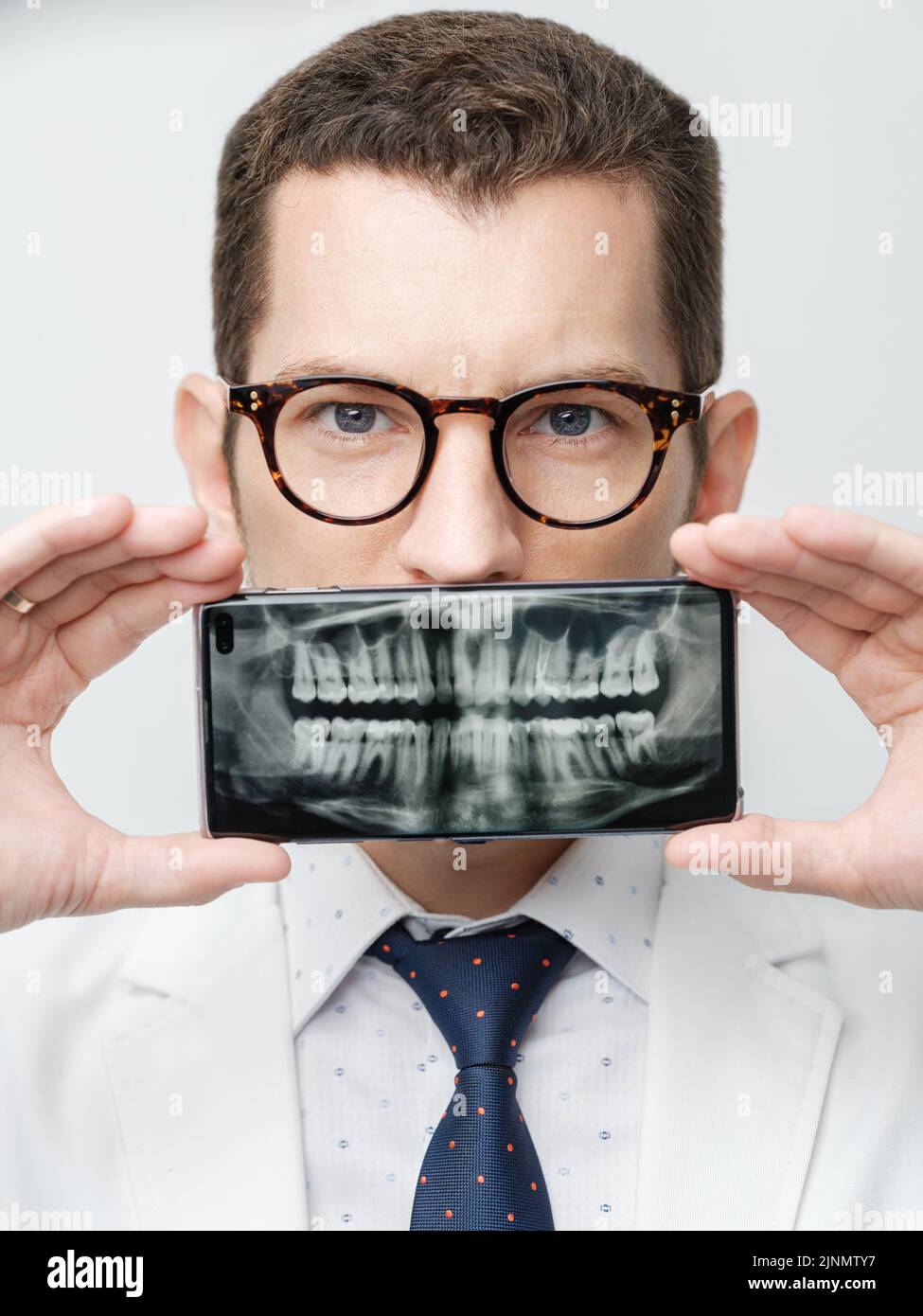 Der männliche Zahnarzt bedeckt seinen Mund mit einem Smartphone, wobei er seine Zähne auf einem Bildschirm des Geräts rönt. Stockfoto