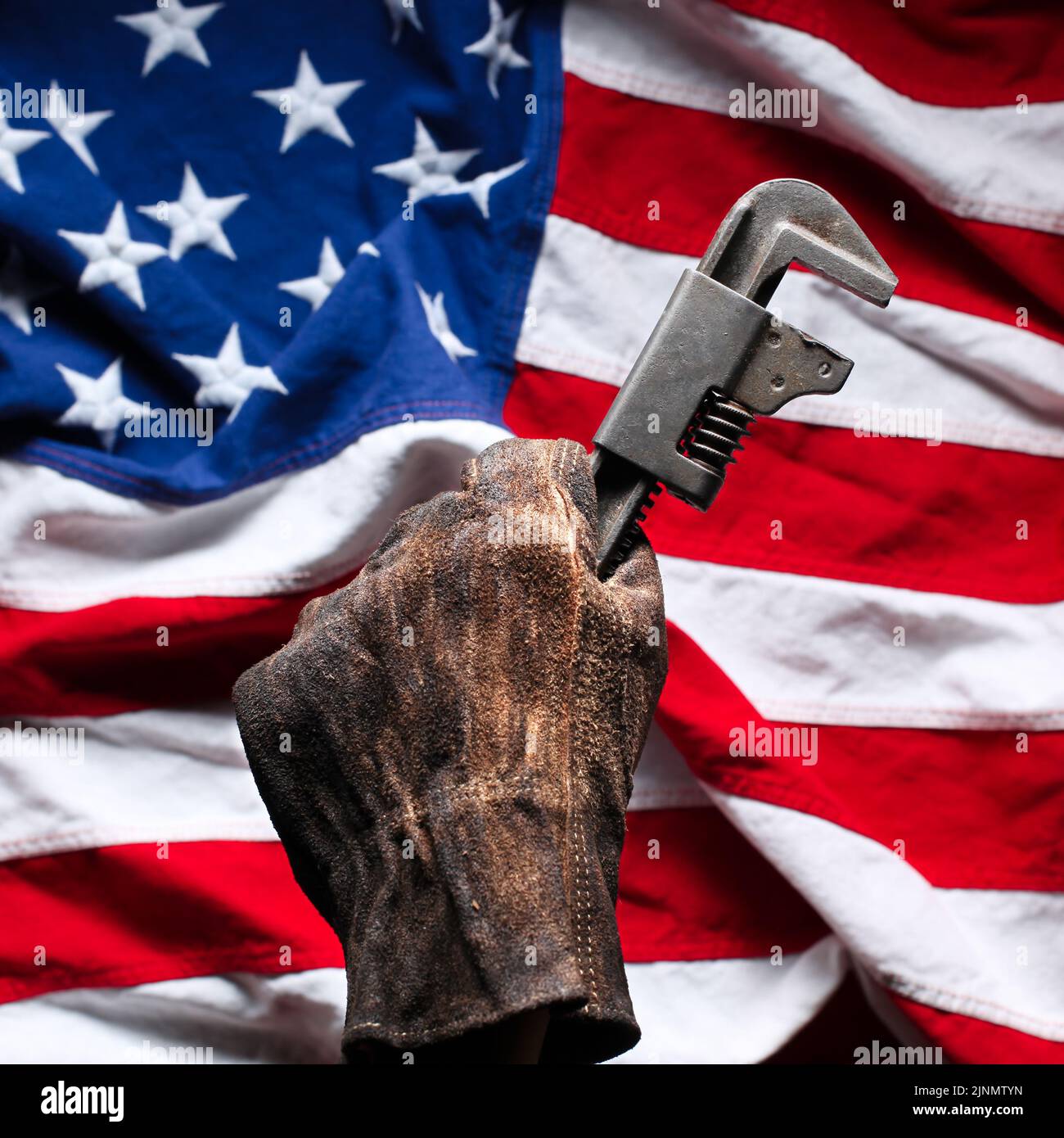 Hand in abgenutzten und schmutzigen Golve halten Rohrschlüssel über American Flag Stockfoto