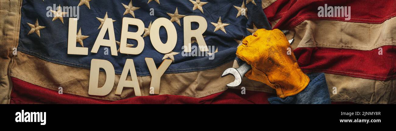 Alte US-amerikanische Flagge, die von einem abgenutzten Arbeitshandschuh mit einem Halbmondschlüssel mit Labour Day-Text gehalten wird. Labor Day und American blue collar worker Konzept. Stockfoto