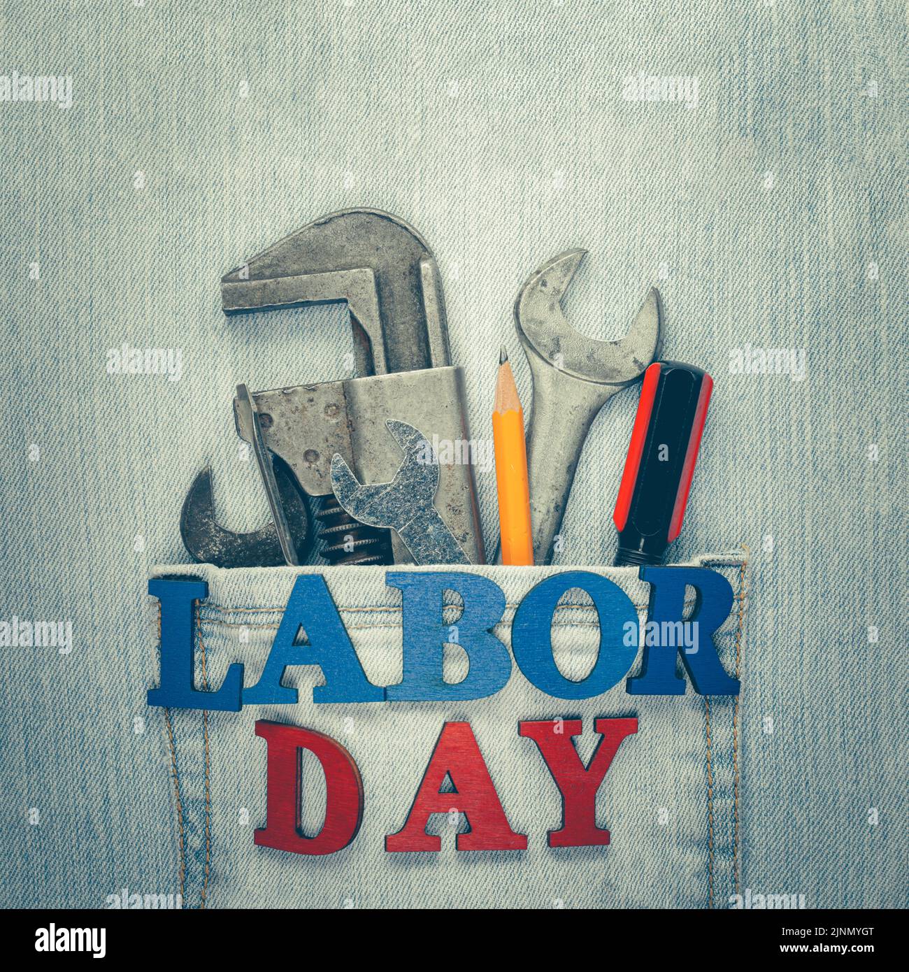 Getragene und verwitterte blaue Jeans mit Arbeitswerkzeugen in der Tasche und Labour Day-Text, der amerikanische Arbeiter feiert. Stockfoto