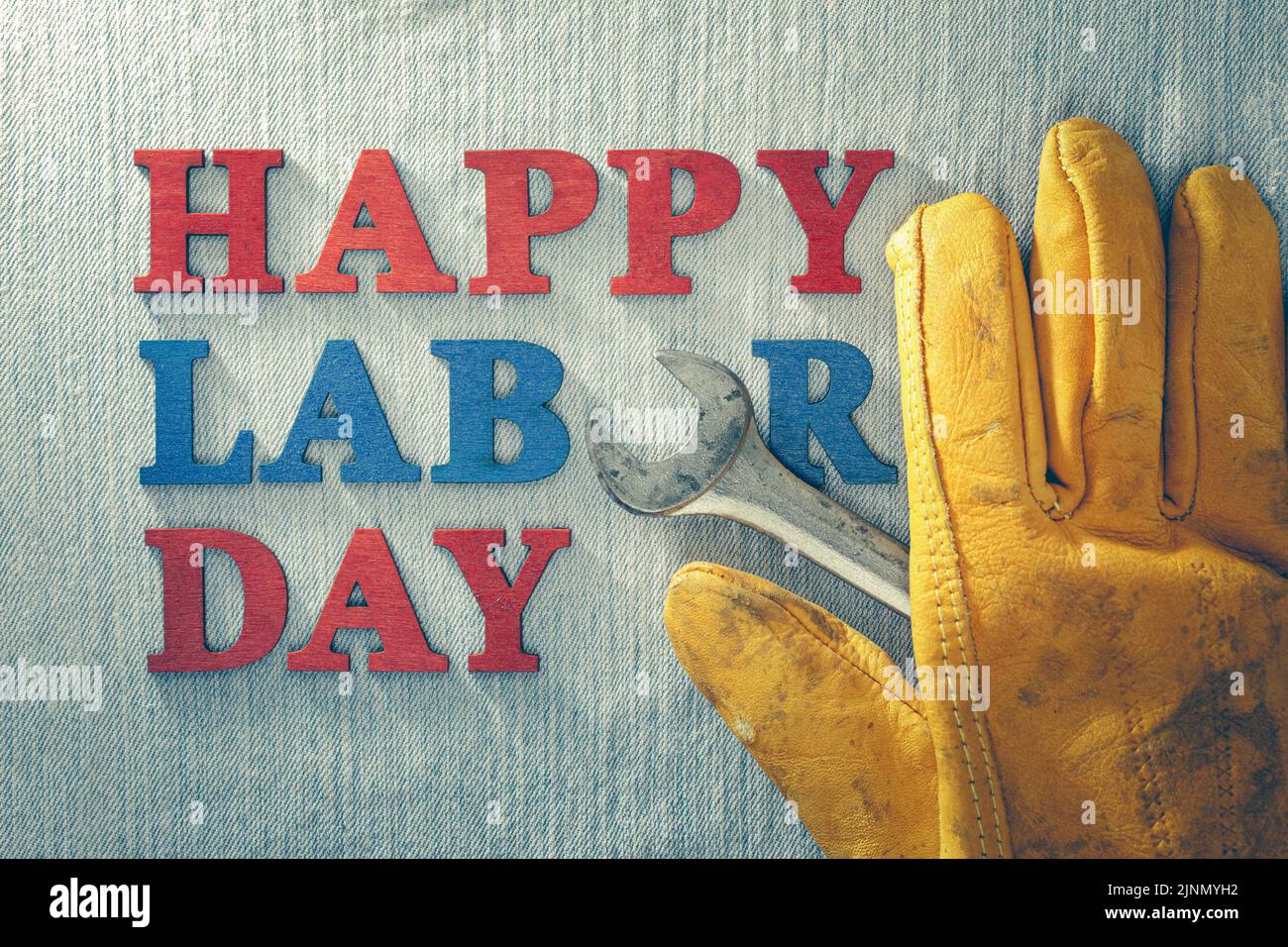 Abgenutzter und verwitterter Arbeitshandschuh und Schraubenschlüssel mit Happy Labor Day-Text, der amerikanische Arbeiter feiert. Stockfoto