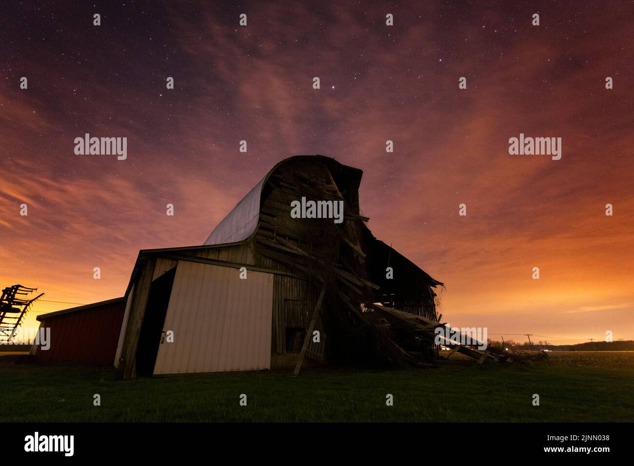 Eine alte runde rote Scheune, die auseinander fällt, sinkt unter den Sternen und Wolken eines sich nähernden Wettersystems weiter. Aufgenommen in Indiana. Stockfoto