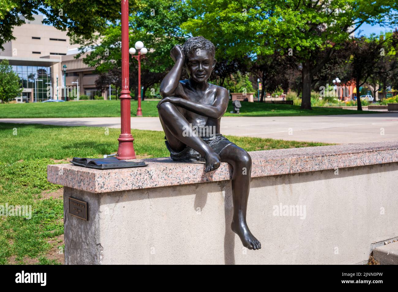 Colorado Springs, CO - 3. Juli 2022: Die Bronzeskulptur "Thinking IT Over" von Betty Sabo zeigt einen gedankenverloren gegangenen Jungen mit einem offenen Buch neben ihm. Stockfoto