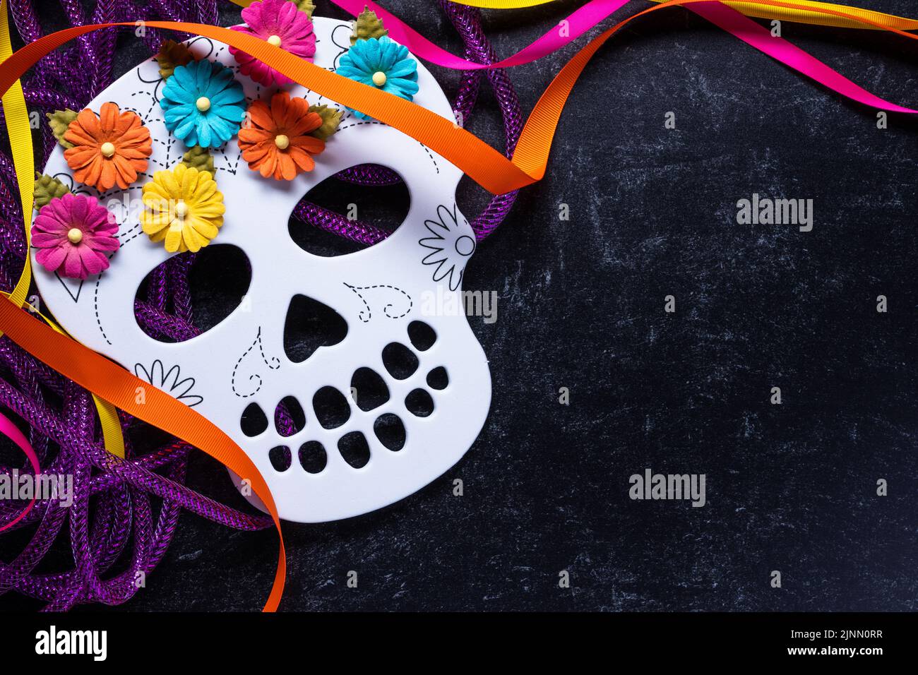 Tag der Toten oder Dia de los Muertos Hintergrund eines weißen Skeletts mit leuchtend rosa orange, gelb und blau Blumen auf einer schwarzen Marmoroberfläche mit m Stockfoto