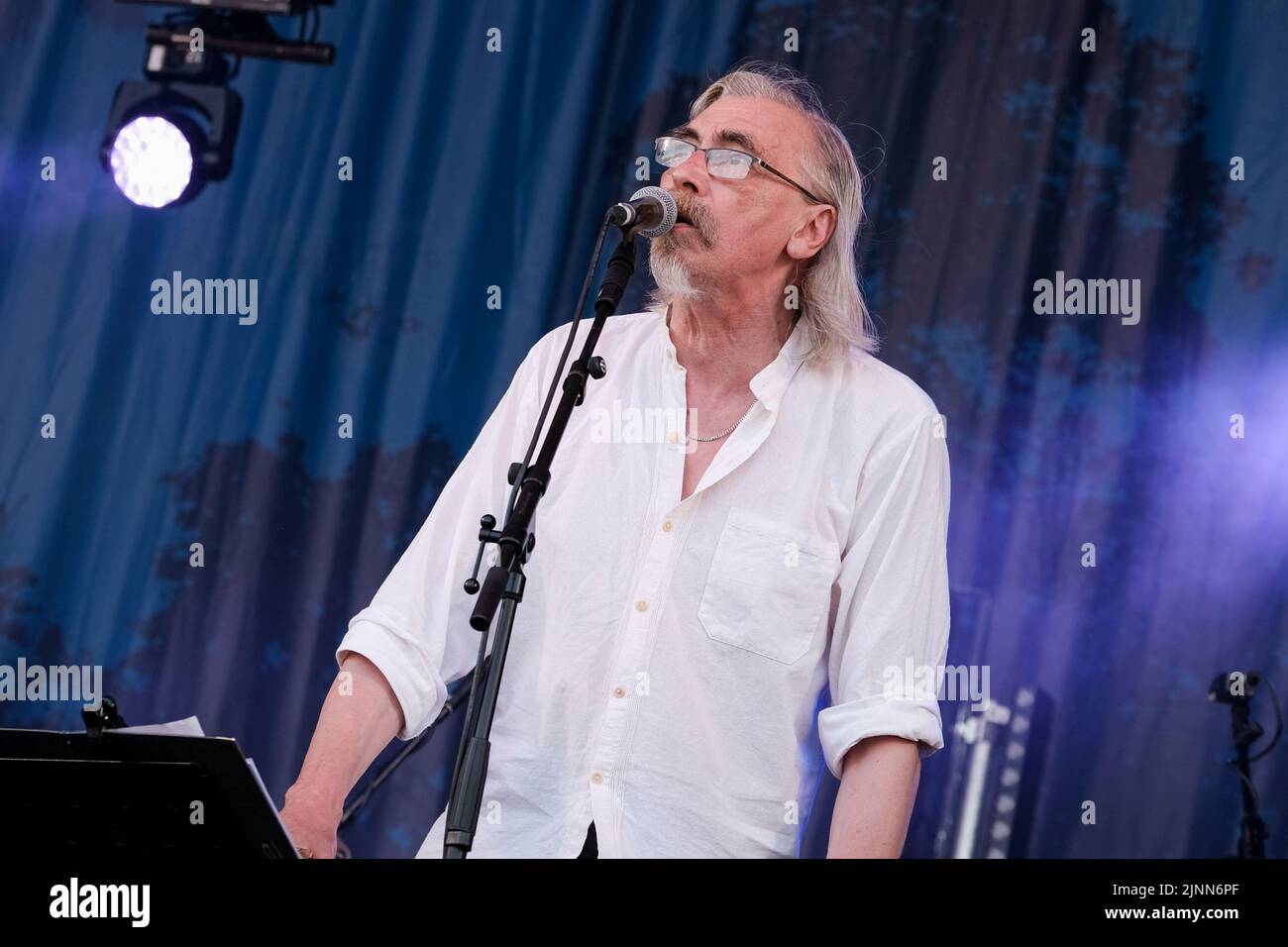 Cropredy, Großbritannien. 12. August 2022. John Tams, englischer Schauspieler, Sänger, Songwriter, Komponist und Musiker und Sohn eines Publikums, ehemaliges Mitglied der Derbyshire Folk-Gruppe Muckram, wacht auf, während die britische Folk-Rock-Gruppe Home Service live auf der Bühne des Cropredy Festivals der Fairport Convention auftrat. Home Service ist eine britische Folk-Rock-Gruppe, die Ende 1980 aus einem Kern von Musikern gegründet wurde, die in Ashley Hutchings' Albion Band gespielt hatten. Ihre Karriere ist allgemein vereinbart, mit dem Album Alright Jack ihren Höhepunkt erreicht zu haben und hat einen Einfluss auf die spätere Arbeit, die John Tams und mehrere andere Mitglieder der Band haben, gehabt Stockfoto