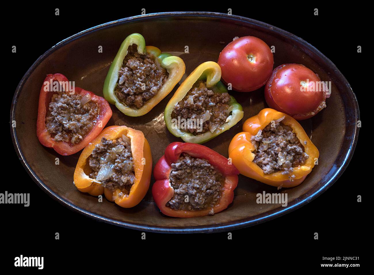 Gefüllte Paprika und Tomaten in einer Kasserolle auf schwarzem Hintergrund, Bayern, Deutschland Stockfoto