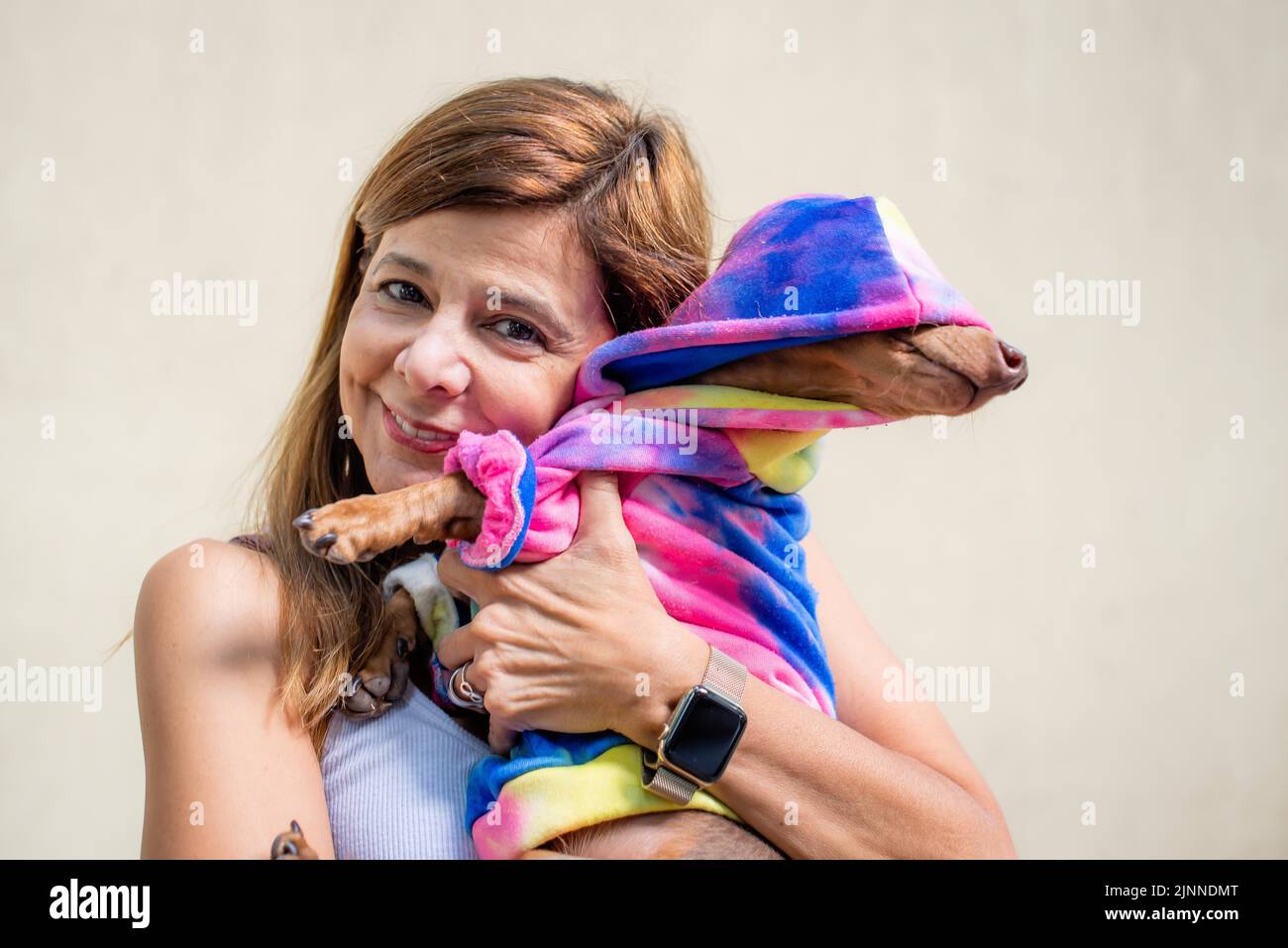 Eine lateinische Frau, die ihren Hund in beiden Kleidern hält. Sie schaut in die Kamera Stockfoto
