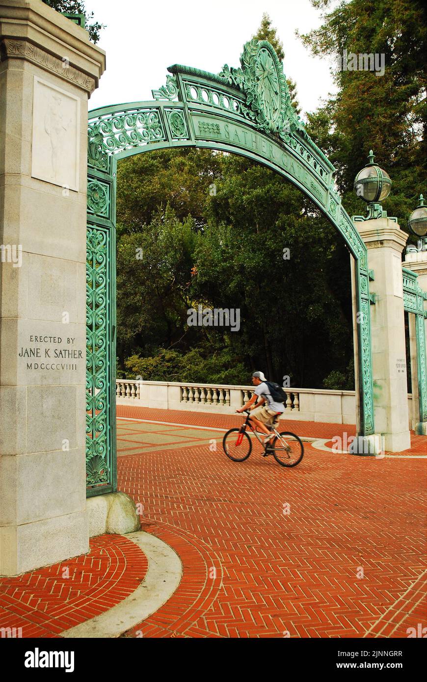 Ein junger Student fährt mit dem Fahrrad durch die historischen Sather Gates, einem Eingang zum Campus der University of California Berkeley Stockfoto