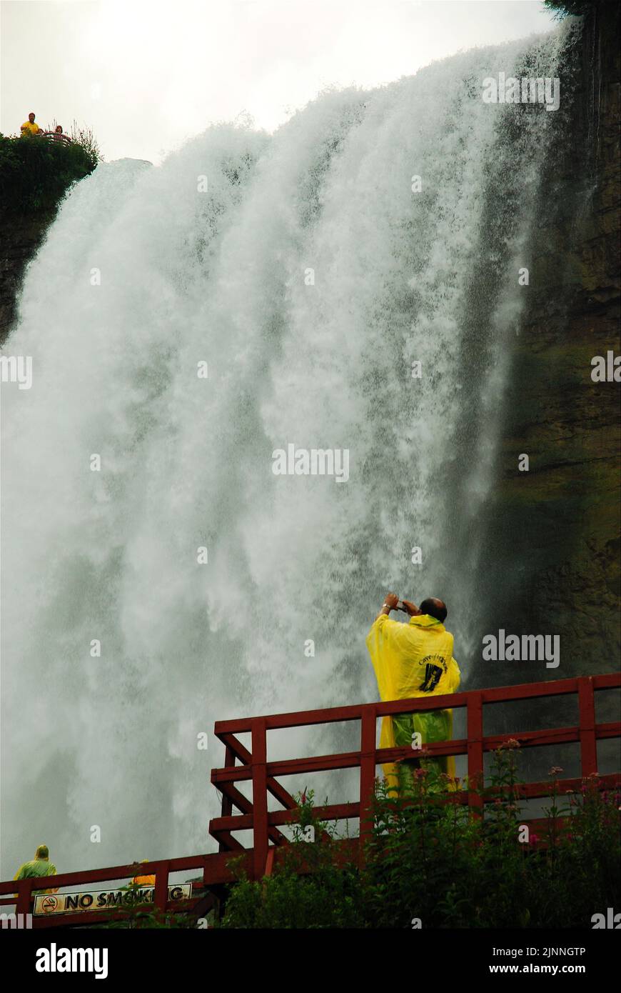 Zwei Besucher in gelben Ponchos erleben die Kraft der Niagarafälle von der Basis aus während der Cave of the Winds Tour Stockfoto