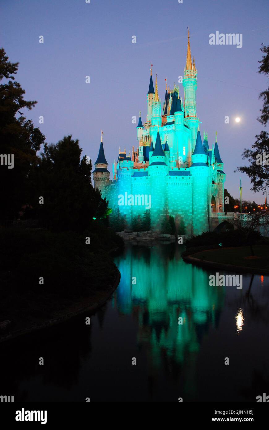 Ein Vollmond erhebt sich über Cinderella's Castle und spiegelt sich in den Gewässern der Lagune im Fantasyland im Magic Kingdom von Walt Disney World bei Nacht wider Stockfoto