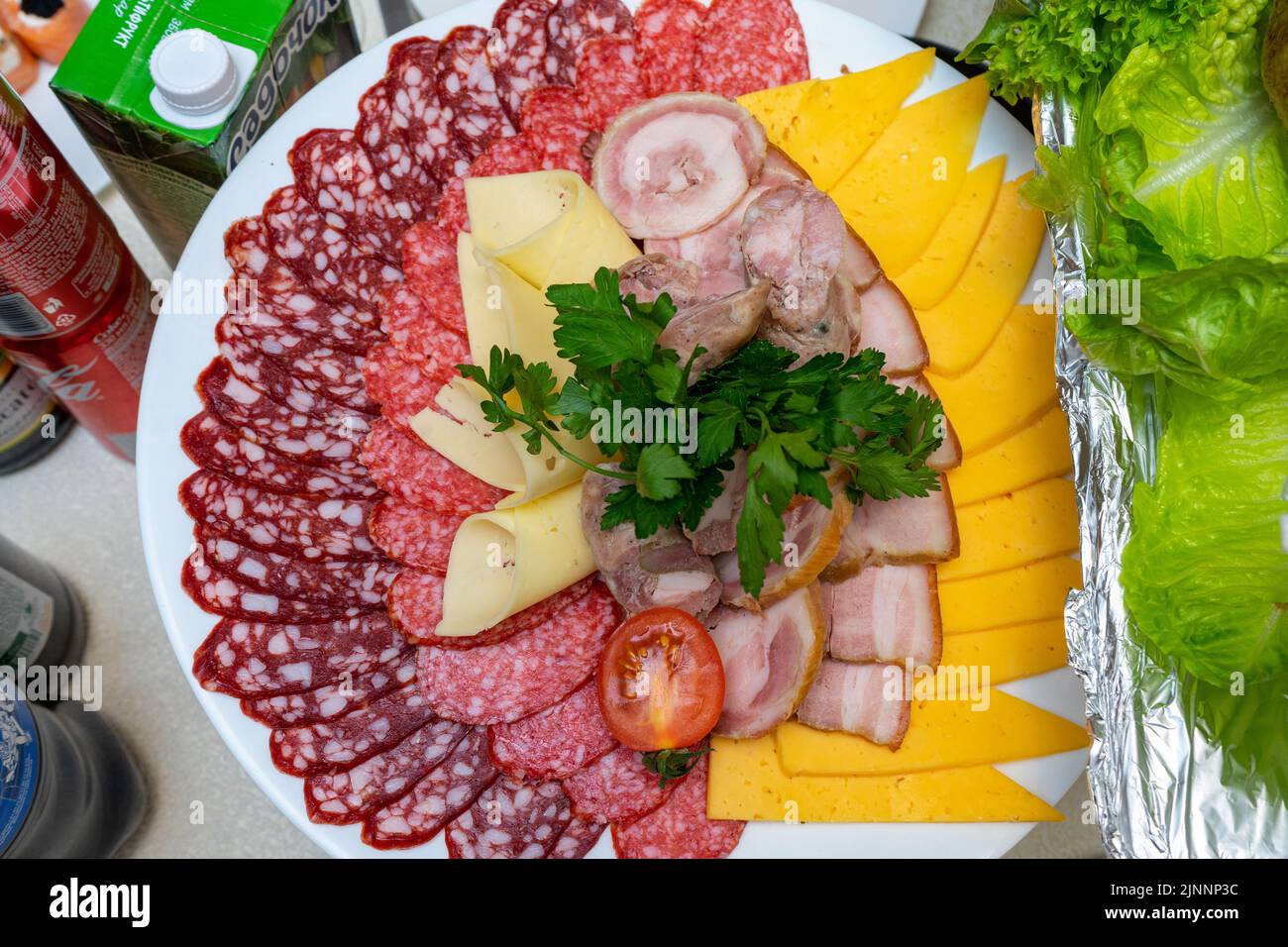 Ein Teller mit kalten Vorspeisen mit verschiedenen Würstchen, Fleisch und Käse. Grünpflanzen und Tomaten. Stockfoto
