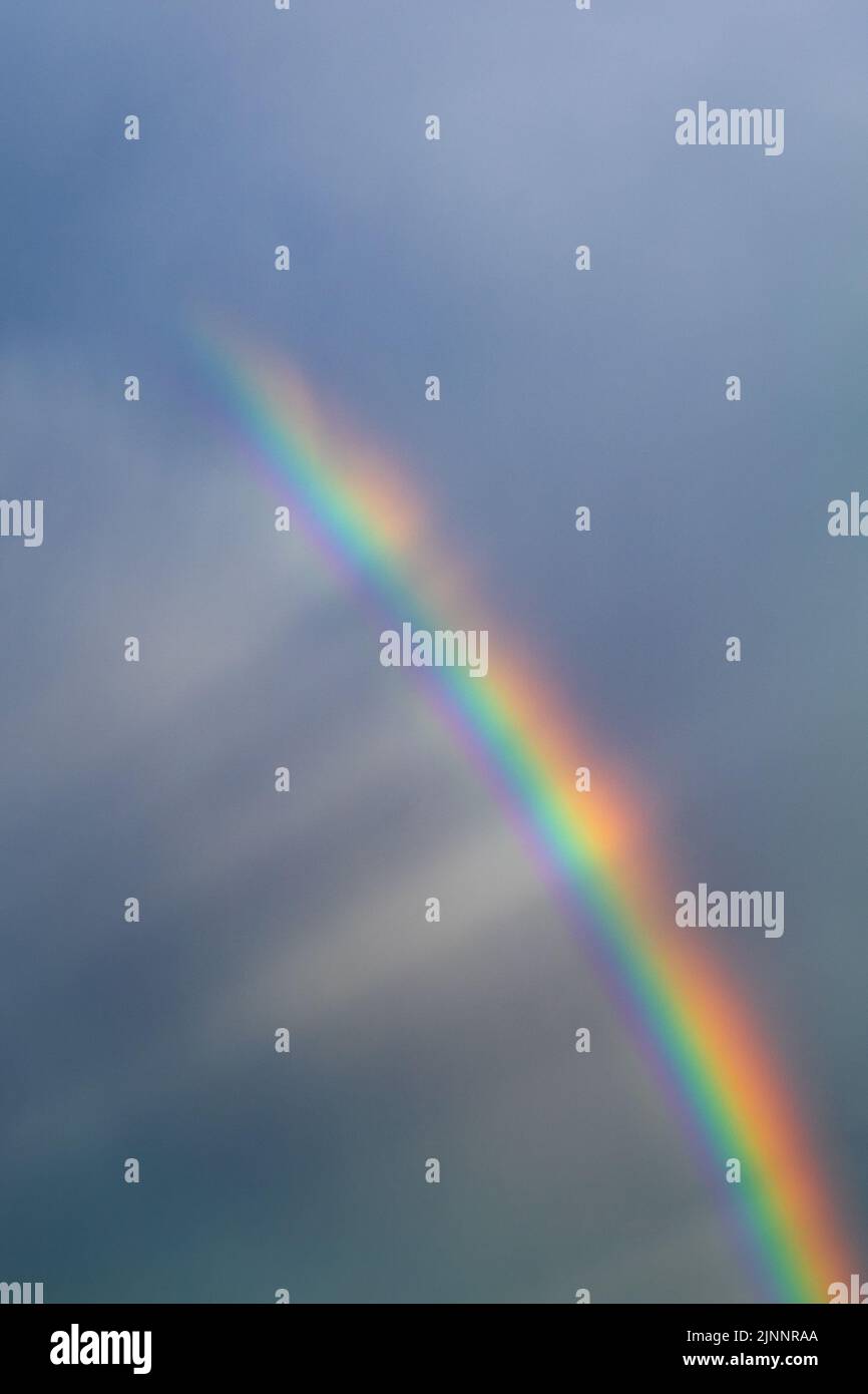 Die Sonnenstrahlen leuchten auf einem mehrfarbigen Regenbogen hinter den Wolken. Vertikales Foto Stockfoto