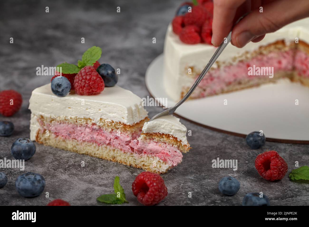 Köstlicher Himbeerkuchen mit Rahm und dekoriert mit frischen Himbeer-Beeren und Minzblättern. Gabel bricht einen Teil des Kuchens ab Stockfoto