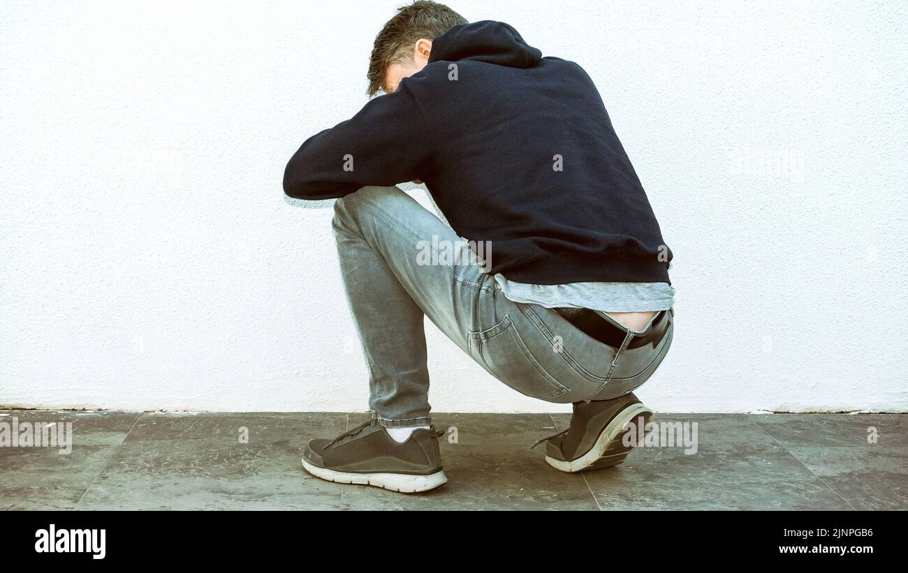 Junger Mann, in Kapuzenhemd und grauen Jeans, sitzend in gebeugt Haltung, stilisierte Bilder. Stockfoto