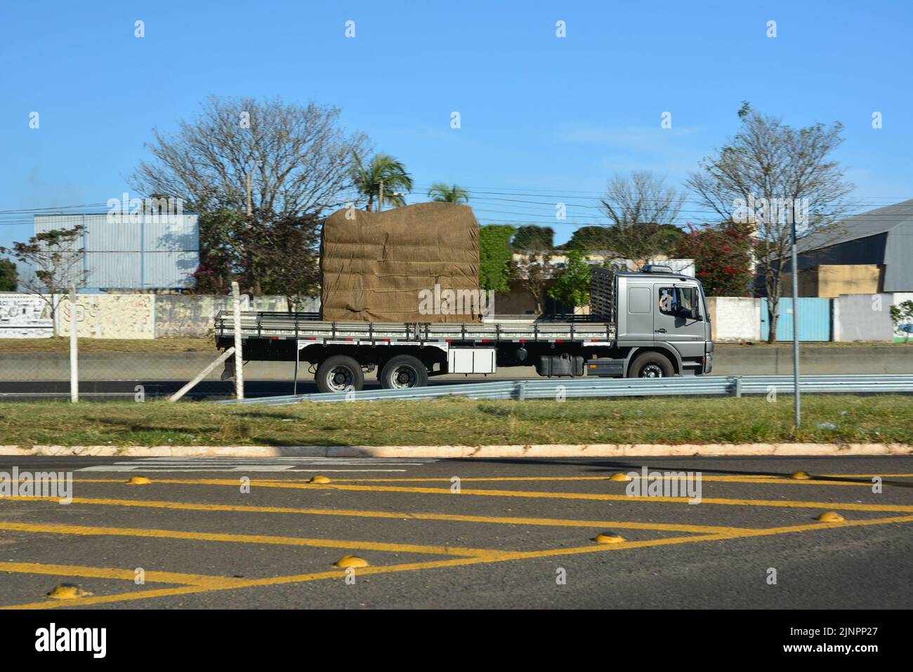 Transport-LKW mit Holzkarosserie auf brasilianischer Autobahn, Seitenansicht, Hintergrund mit absichtlichen Unschärfen, Asphalt im Vordergrund mit Landschildern, Autobahn in ur Stockfoto