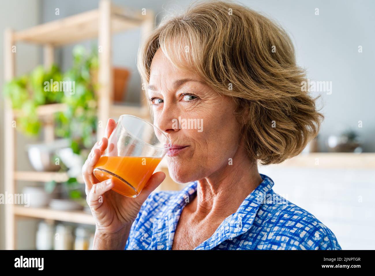 Schöne reife ältere Frau zu Hause, häusliches Leben und Freizeit Momente - 50-60 Jahre alt hübsche weibliche Erwachsene trinken gesunden Orangensaft für die Pause Stockfoto