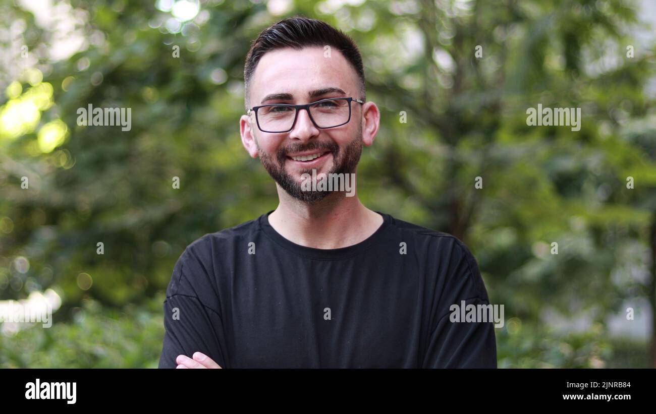 Porträt eines jungen, gutaussehenden Mannes mit Bart und Brille. Junger Mann im schwarzen Hemd lächelt und schaut in die Kamera. Outdoor Natur Hintergrund Stockfoto