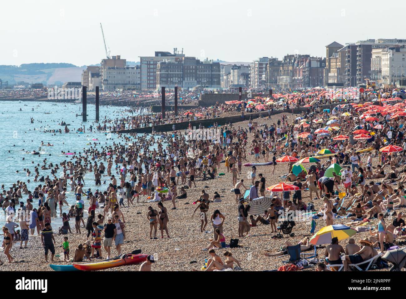 Brighton, Großbritannien. 13. August 2022. Tausende strömten diesen Samstag nach Brighton Beach und machten das Beste aus dem heißen Wetter. Ein See mit roten Schirmen (gesponsert von Walls Ice Cream) kann gesehen werden, die sich von Brighton bis Hove erstrecken Kredit: @Dmoonuk/Alamy Live News Stockfoto