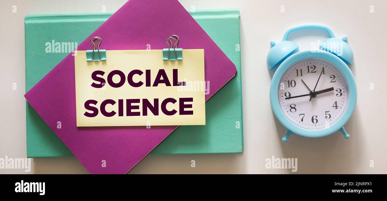 Sozialwissenschaftliches Memo auf einem Notizblock, neben einer Uhr auf weißem Hintergrund Stockfoto