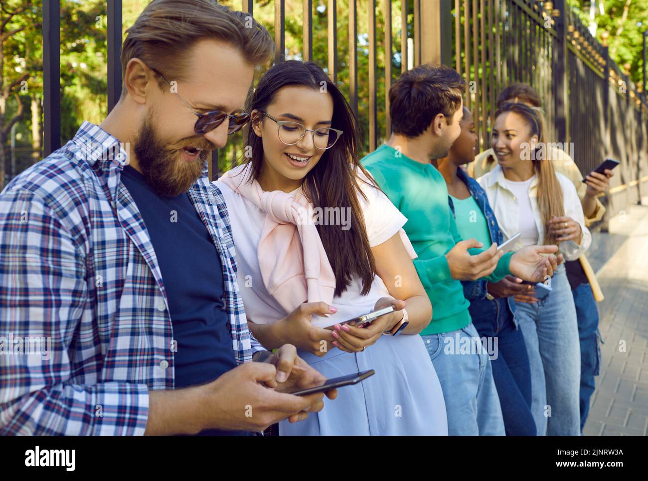 Glückliche junge, vielfältige Menschen, die auf der Straße der Stadt stehen und ihr Mobiltelefon benutzen Stockfoto