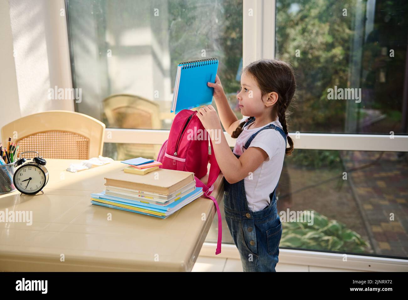 Das kleine europäische Kind, ein intelligentes Schulmädchen, das ihre Schulmaterialien in eine pinke Schultasche legt. First-Grader-Klasse. Zurück zur Schule Stockfoto