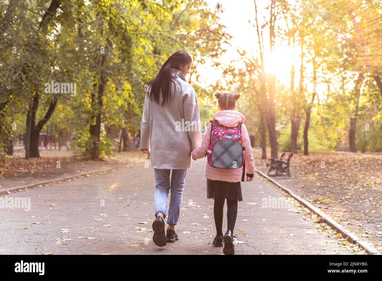 Mutter und Tochter gehen im Herbstpark spazieren. Kleines Mädchen nach der Schule mit Mutter von hinten. Alltag Stockfoto