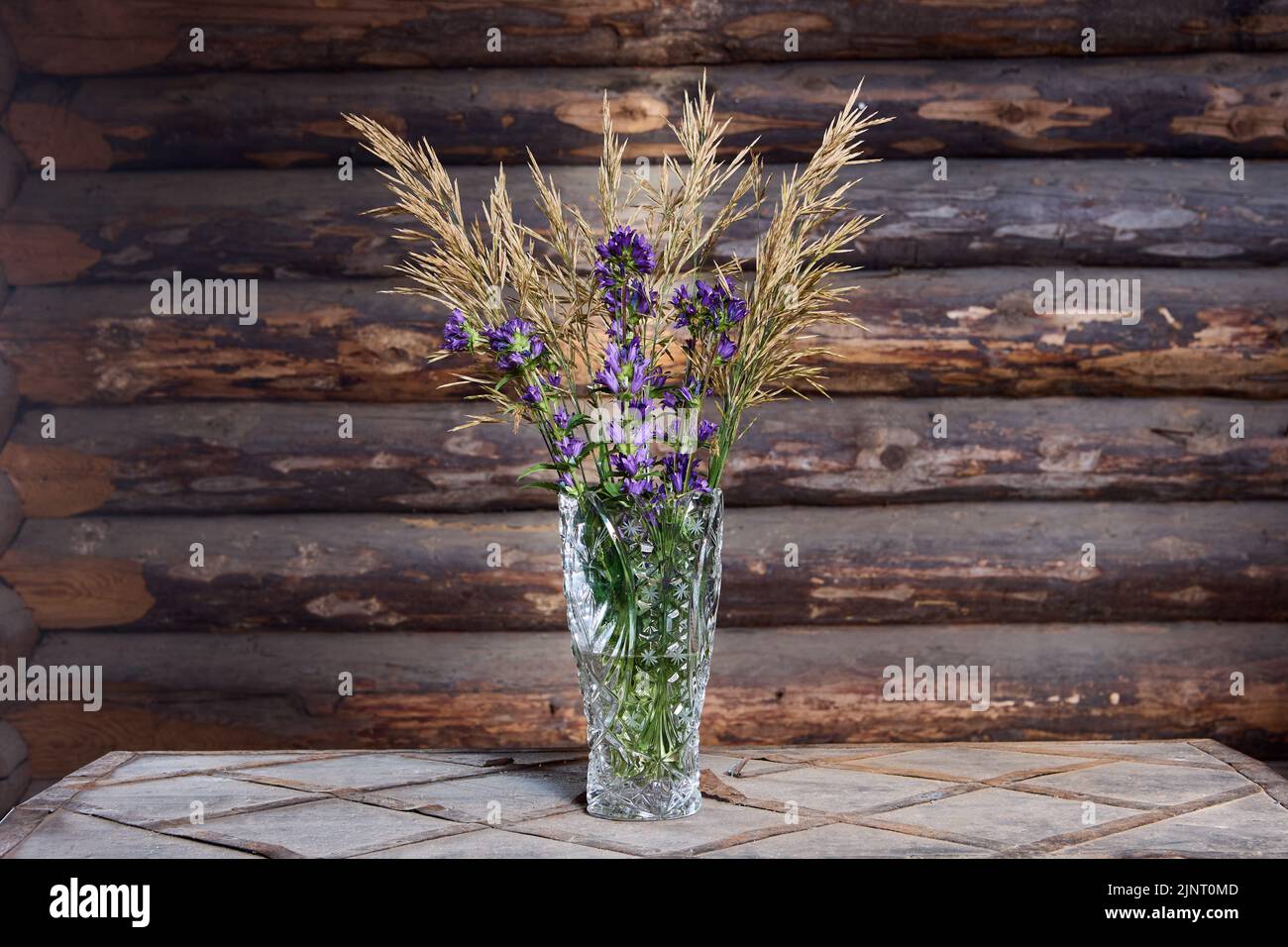 Bouquet Komposition aus Garten Lupine Blumen und Wildwiese festcue Gras in Kristallvase auf rustikalem Tisch. Stockfoto