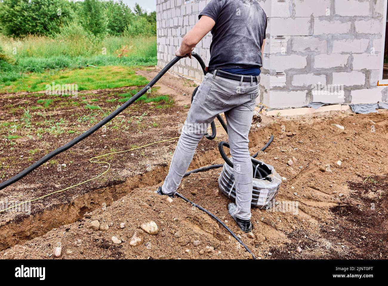 Der Bauarbeiter verkabelt im Graben, er legt das Stromkabel am Boden des Grabens ab. Stockfoto