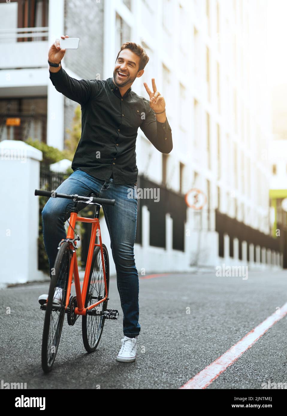 Frieden raus. Ganzkörperaufnahme eines hübschen jungen Mannes, der Selfies macht, während er mit dem Fahrrad durch die Stadt fährt. Stockfoto