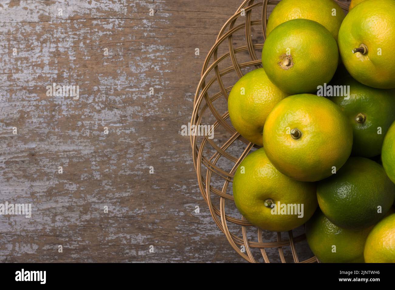 Süße orange Früchte in einem Korb, auf rustikale Holztischplatte platziert, direkt von oben mit Platz für Text genommen Stockfoto