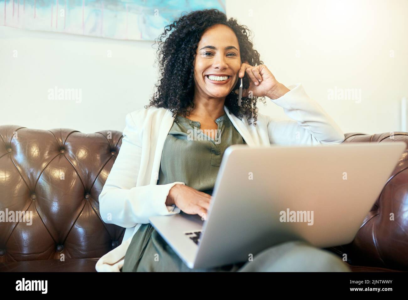 Die meisten meiner Kunden hören online von mir. Eine Frau, die mit ihrem Laptop auf dem Sofa sitzt. Stockfoto