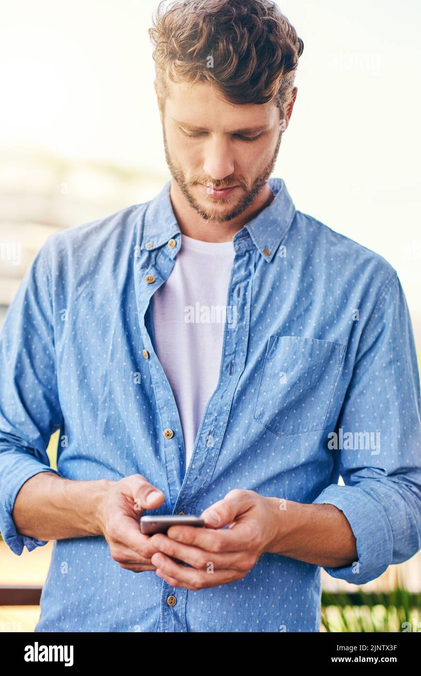 Oh je, ist das die Zeit. Ein selbstbewusster junger Mann, der tagsüber draußen auf seinem Handy SMS schreibt. Stockfoto