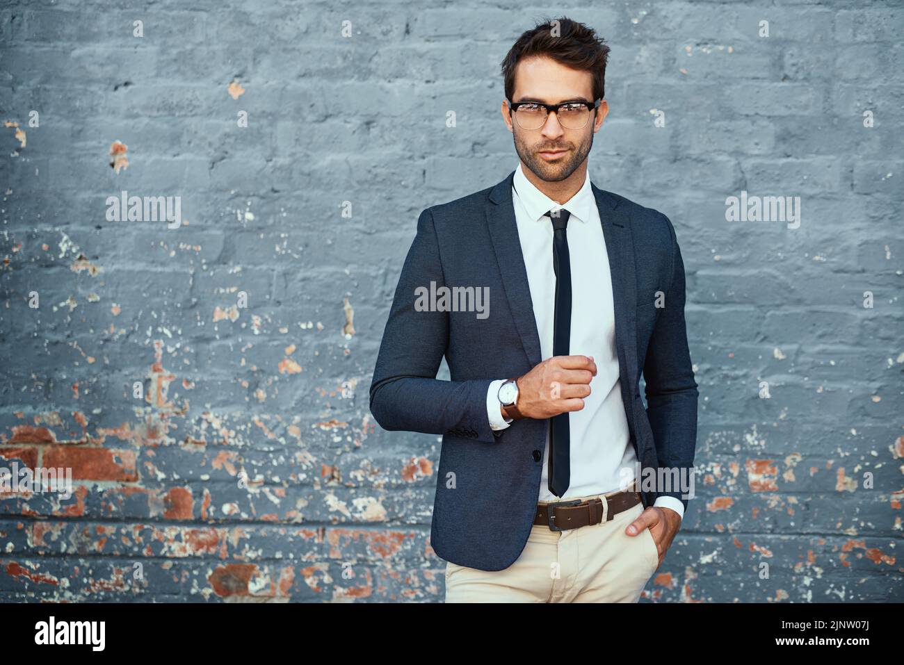 Ich ziehe mich immer an, um zu beeindrucken. Ein Porträt eines hübschen jungen Geschäftsmannes, der vor einer grauen Backsteinmauer steht. Stockfoto