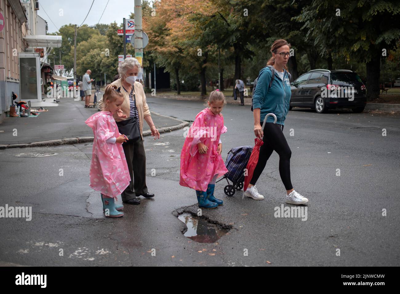 Belgrad, Serbien, 13. Aug 2022: Zwei Mädchen auf einem Spaziergang mit Mama und Oma, die eine herzförmige Pfütze beobachten Stockfoto