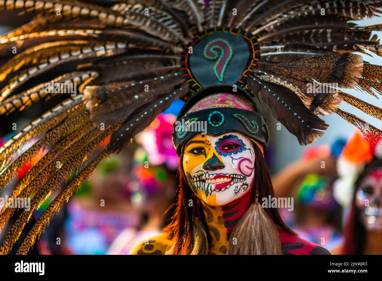 Ein mexikanisches Mädchen, bekleidet als La Catrina und mit einem Kopfschmuck aus aztekischen Federn, nimmt an den Feierlichkeiten zum Tag der Toten in Taxco, Mexiko, Teil. Stockfoto