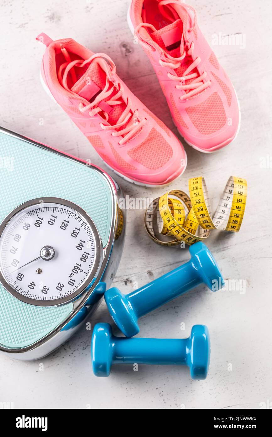 Waage, Trainer und Kurzhanteln mit Maßband auf dem Boden. Sport- und Fitnessgeräte auf einer Etage - Blick von oben. Stockfoto