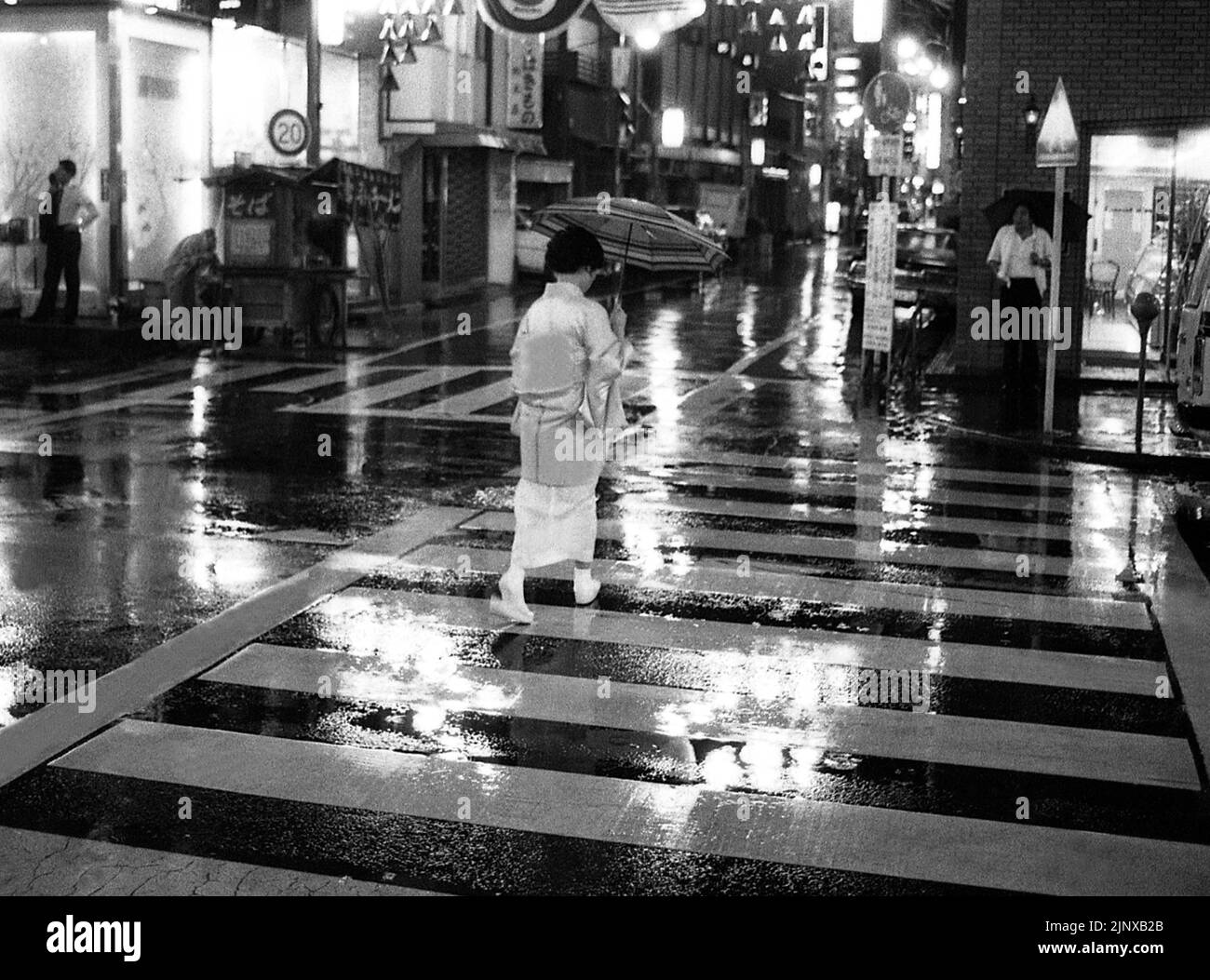 TOKIO JAPAN Frau in traditioneller Kleidung und Regenschirm geht an einem regnerischen Abend über eine Straße in Tokio Stockfoto