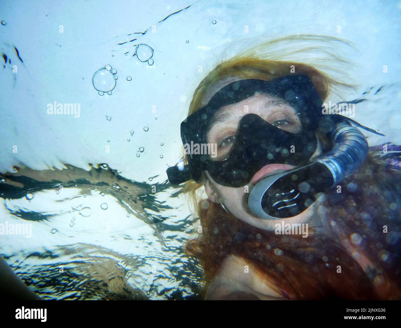 Frau mit Schnorchelmaske unter Wasser, die die Kamera anschaut Stockfoto