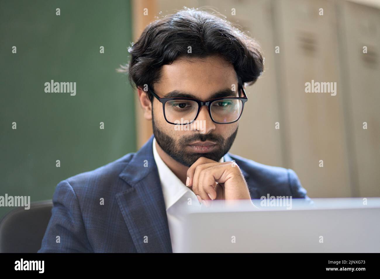 Nachdenklicher junger indischer Geschäftsmann, der Marktdaten analysiert und Computer betrachtet. Stockfoto