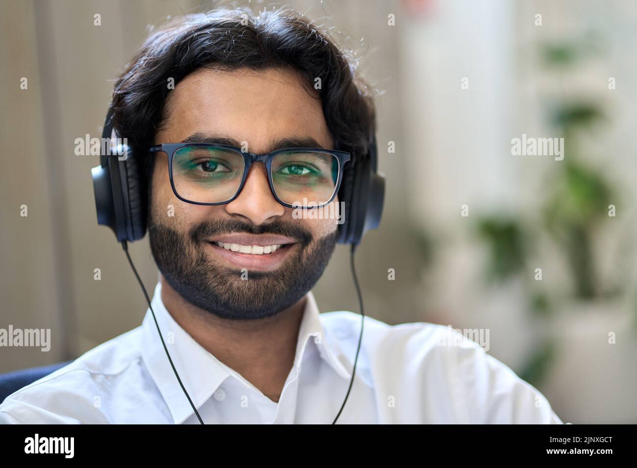 Lächelnder indischer Geschäftsmann trägt Kopfhörer und blickt auf die Kamera, ein Kopfbildnis. Stockfoto