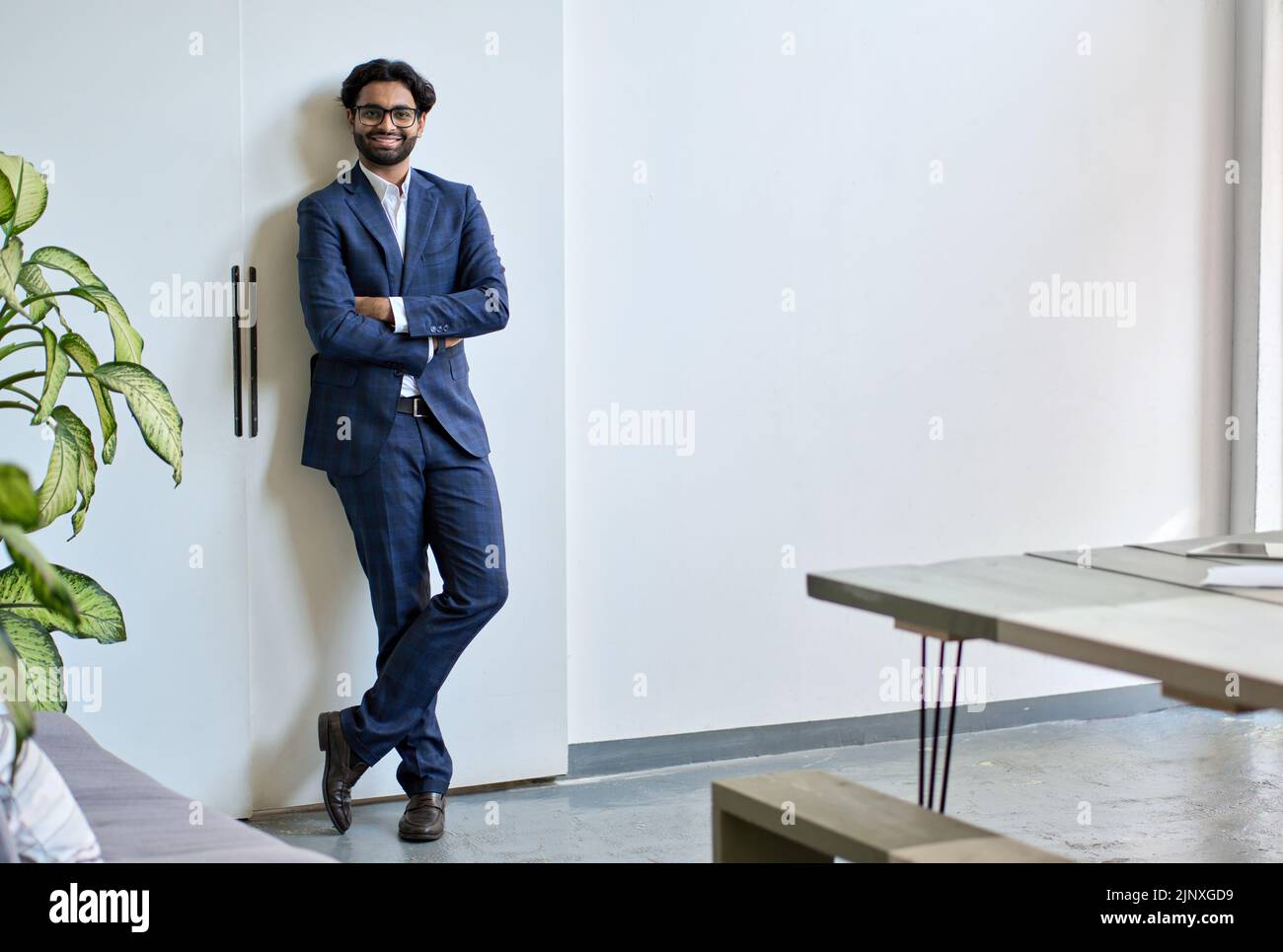 Lächelnder junger indischer Geschäftsmann trägt Anzugständer im Büro, Porträt. Stockfoto